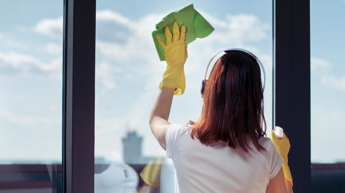 Frau putzt Fenster mit Putzhandschuhen