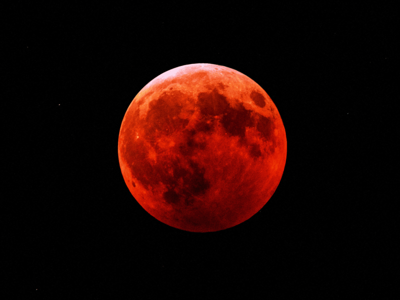 Roter Vollmond in dunklem Nachthimmel.