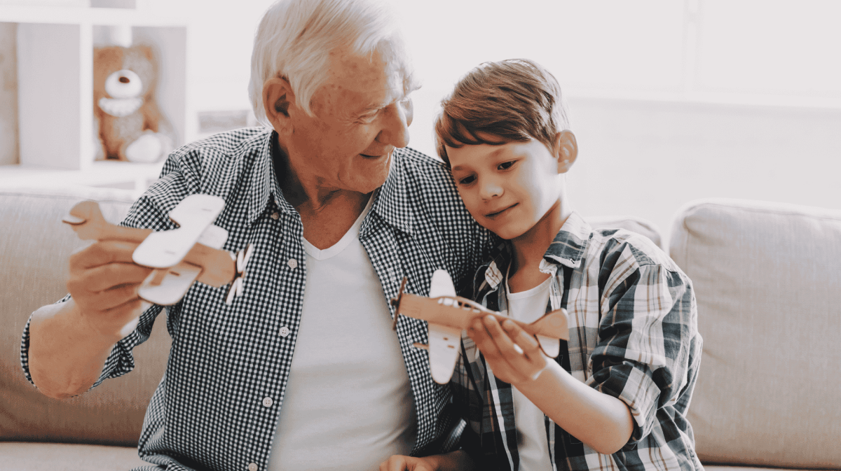 Ein Opa spielt mit seinem Enkelsohn mit gebastelten Flugzeugen.