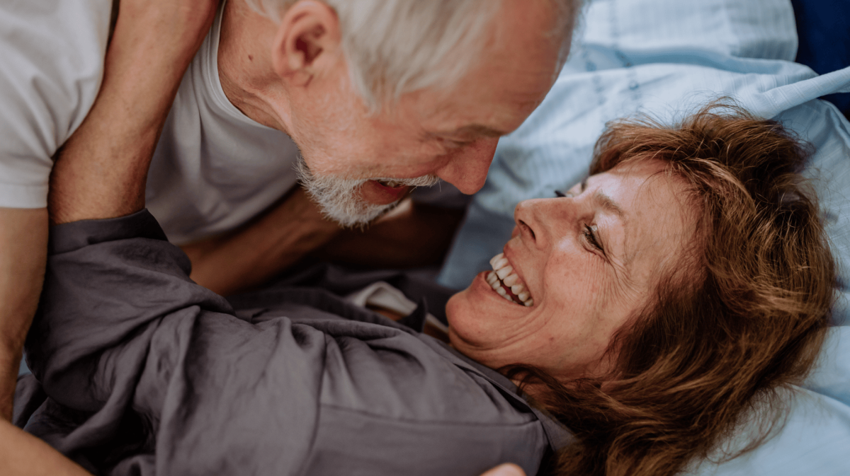 Verliebtes, älteres Paar liegt zusammen im Bett.