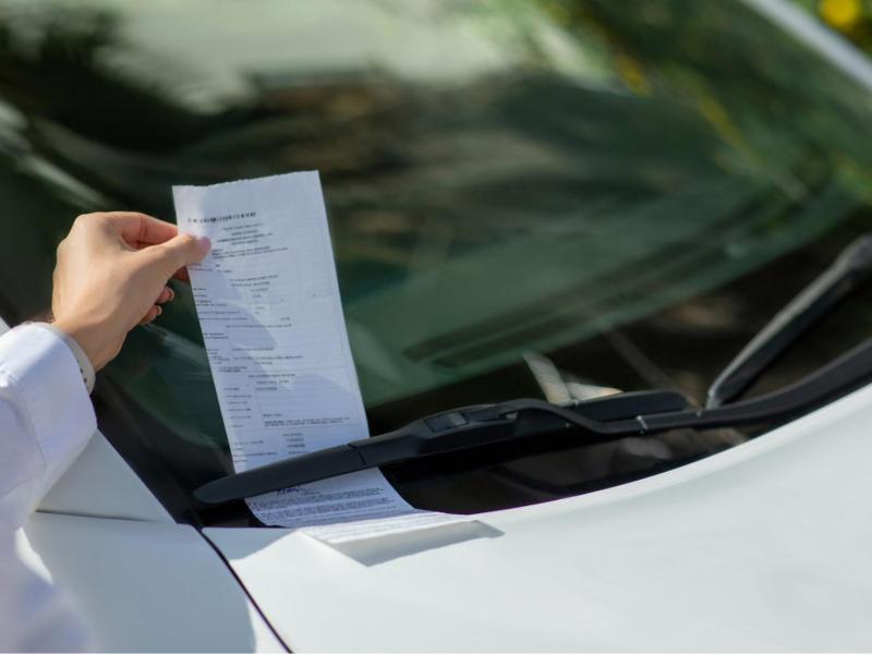 Frau zieht ein Knöllchen unter den Scheibenwischern hervor.