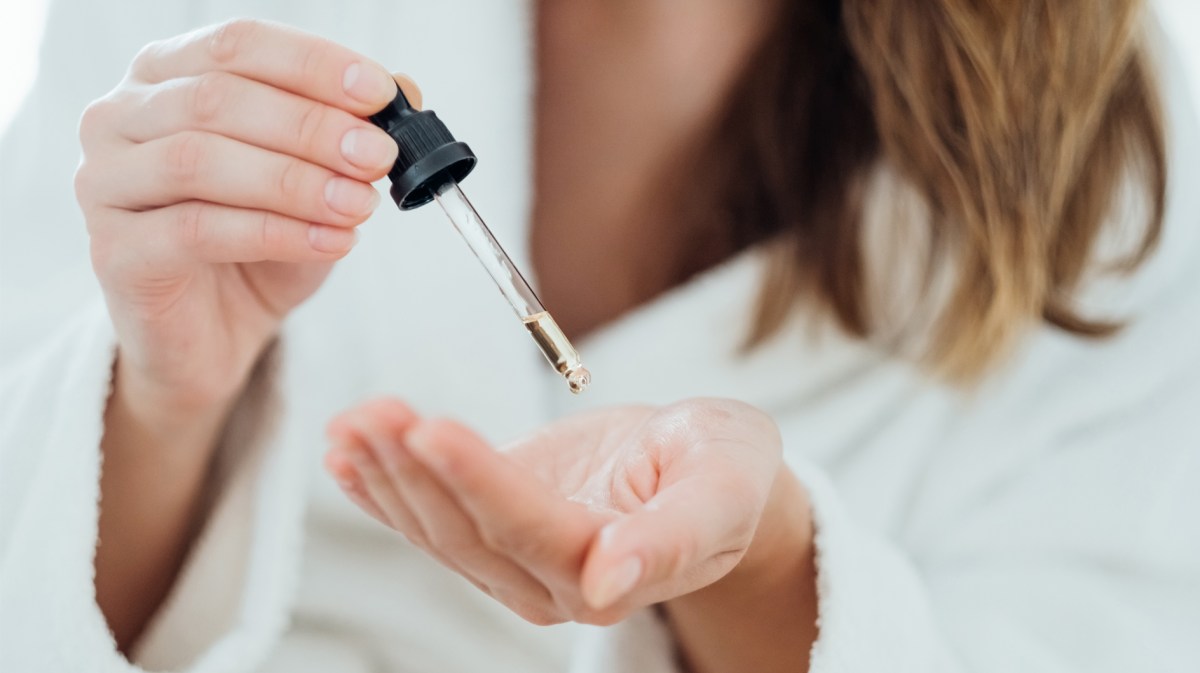 Frau die sich ein Serum mit einer Pipette in die Hand tropft.