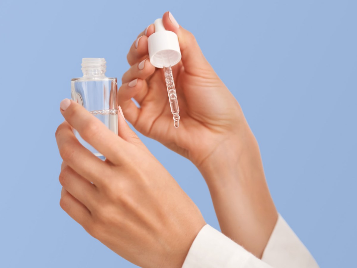 Zwei H&auml;nde mit einem Serum aus dem ein Tropfen auf die H&auml;nde f&auml;llt.