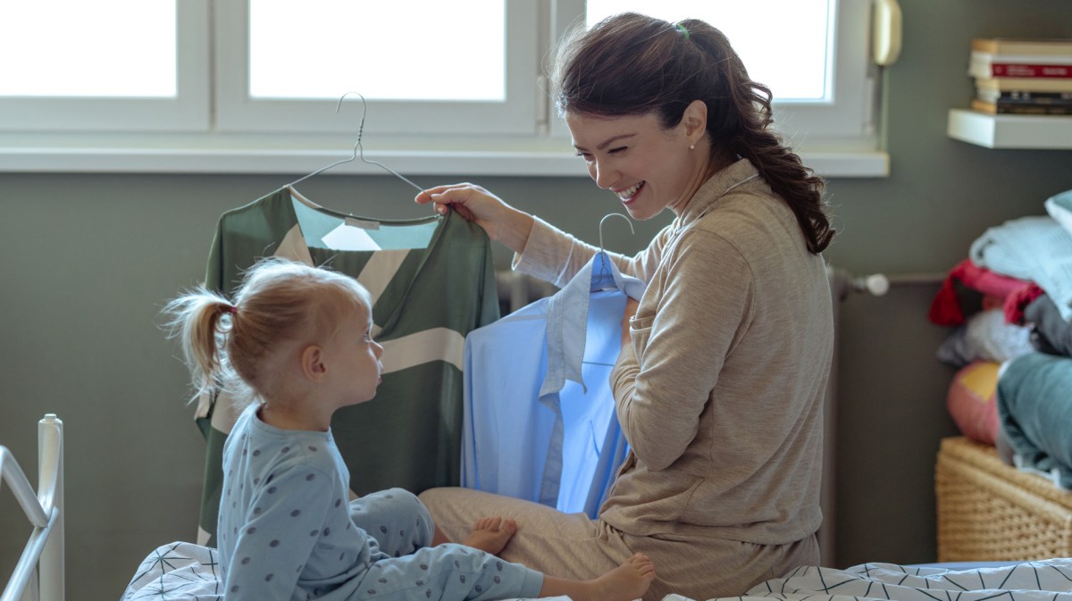 Frau, die mit ihrem Kind auf dem Bett sitzt und überlegt, was sie anzieht.