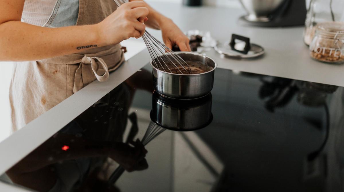 Eine Frau kocht eine Flüssigkeit im Topf auf einem Induktionsherd aus und rührt mit einem Schneebesen um.