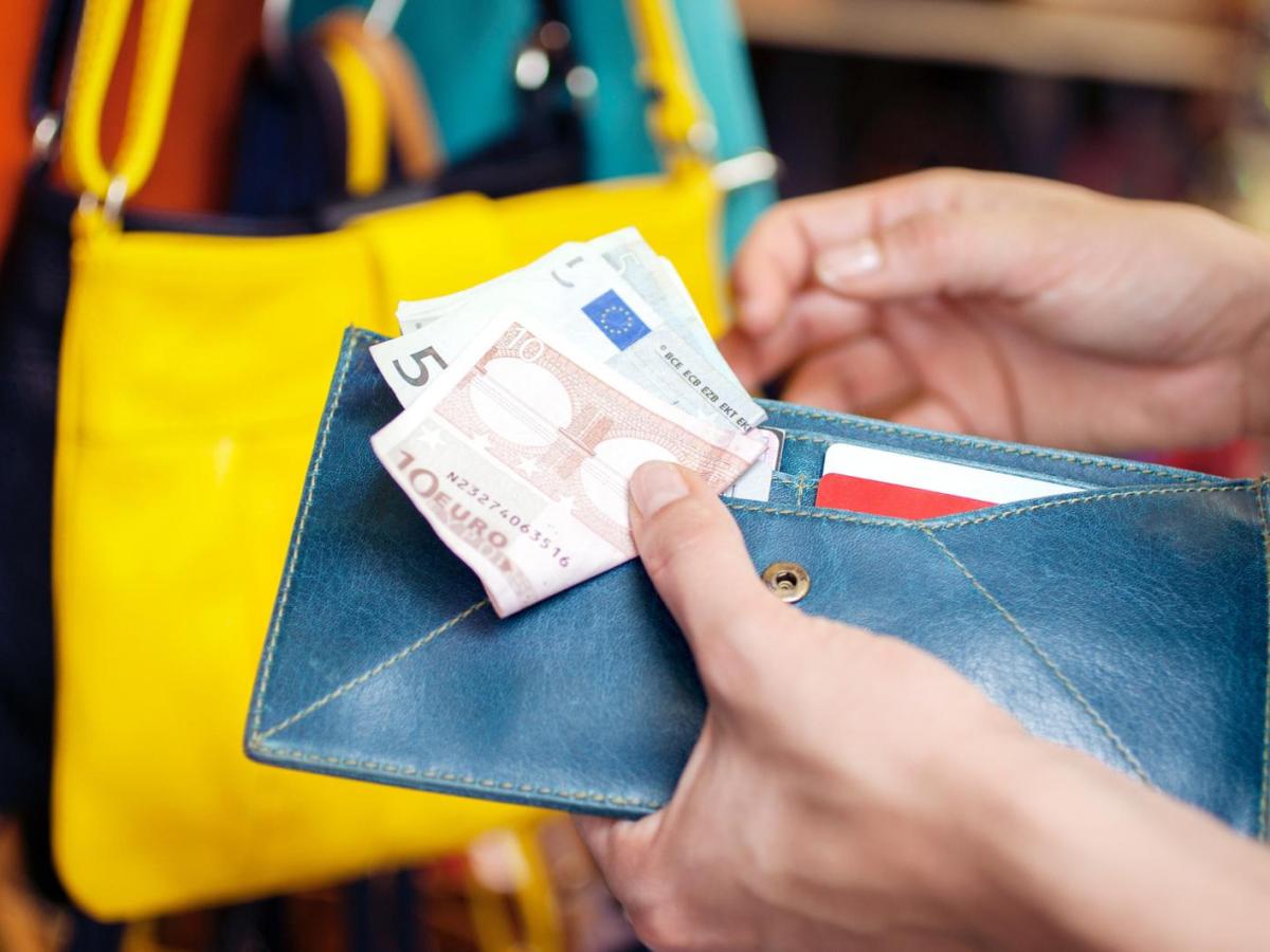 Frau hält ihr Portemonnaie und 15 Euro in Scheinen in der Hand beim Einkaufen.