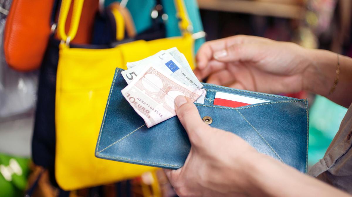 Frau hält ihr Portemonnaie und 15 Euro in Scheinen in der Hand beim Einkaufen.