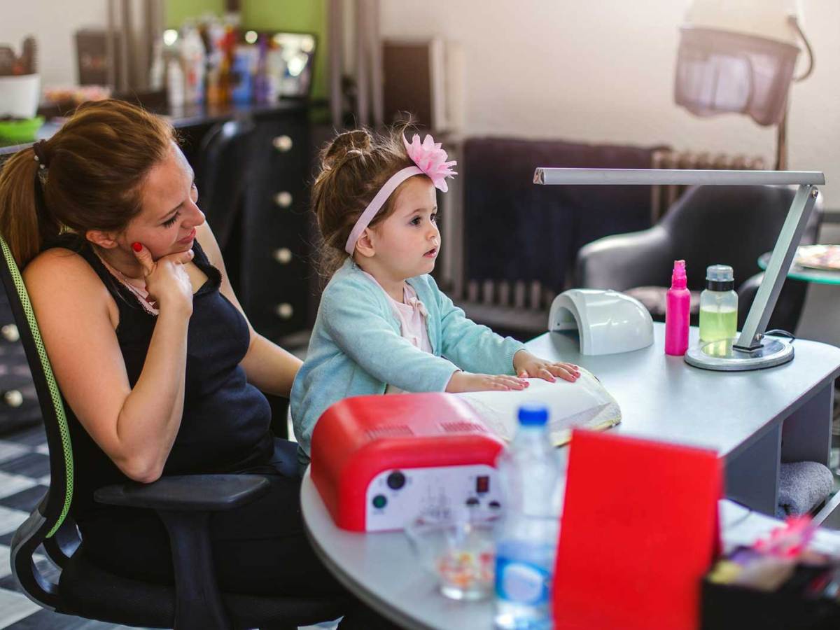 Kind sitzt auf dem Schoß der Mutter in einem Nagelstudio am Behandlungstisch.