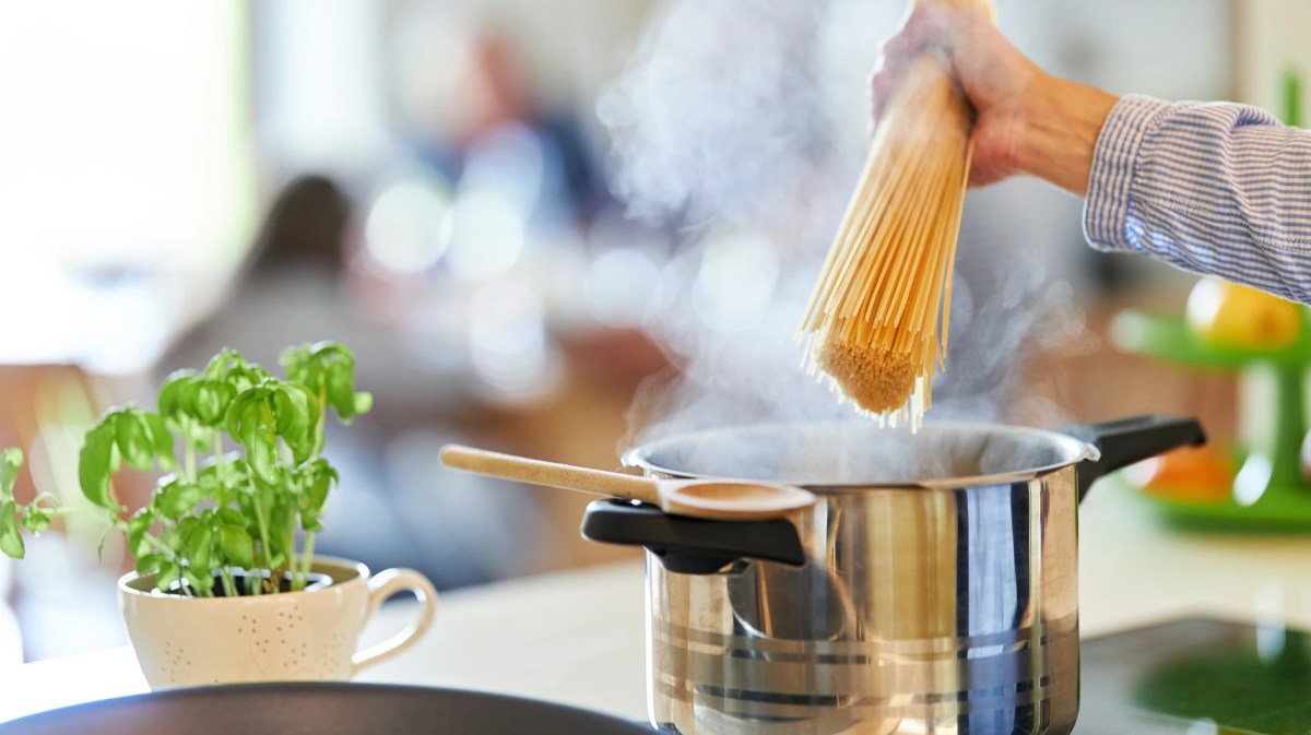 Nahaufnahme einer Hand, die Spaghetti in einen Topf auf dem Herd gibt.