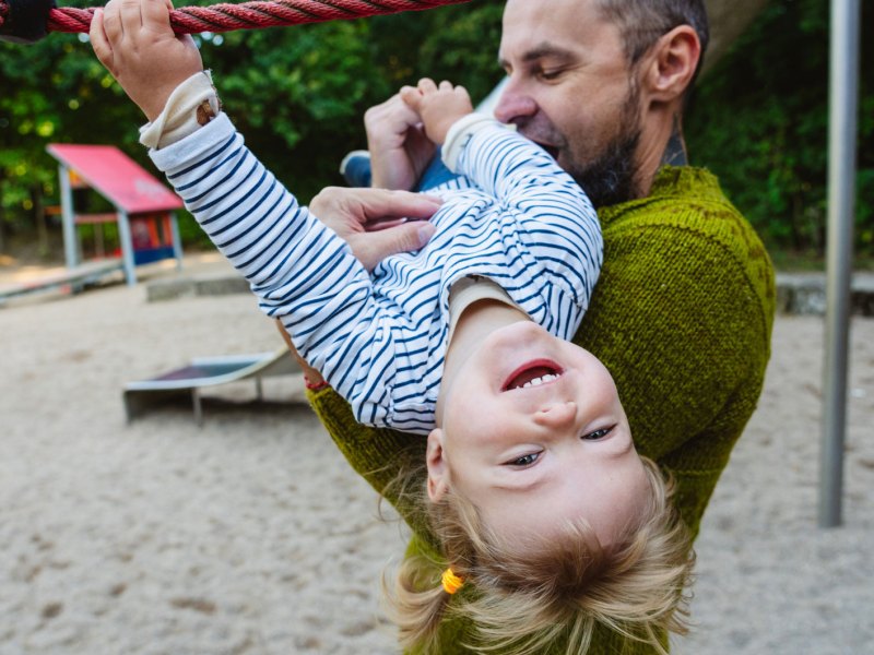 Papa und Tochter toben auf dem Spielplatz herum.