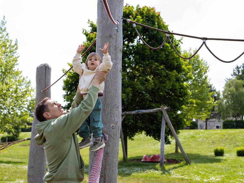 Vater hilft seinem ca. 4-jährigen Kind an ein Klettergerüst.