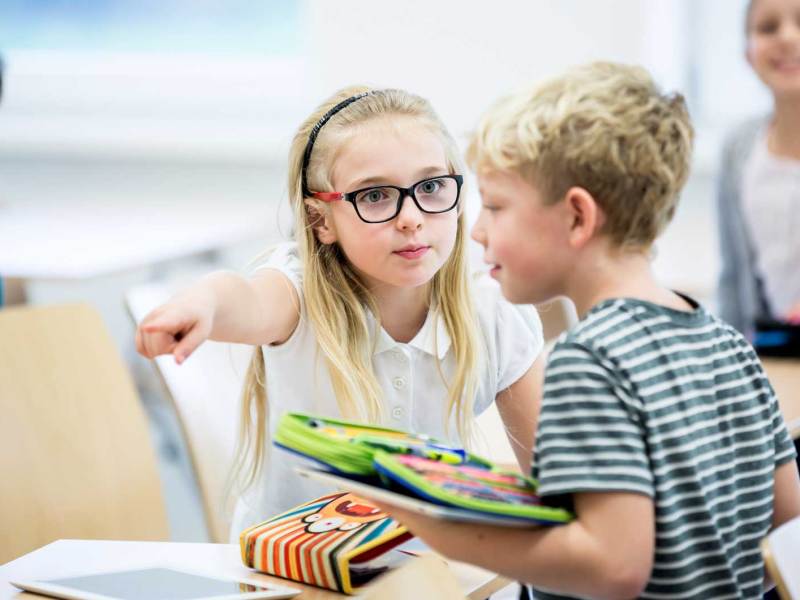 Ein Mädchen zeigt ihrem Mitschüler, wohin er sich setzen soll.