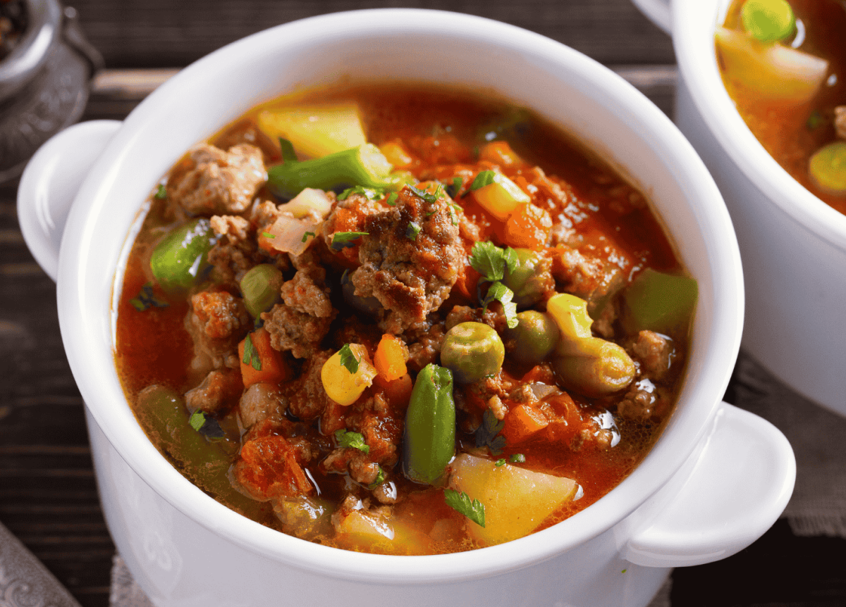 Suppe mit Hackfleisch, Gemüse und Kartoffeln in kleiner, weißer Schüssel.