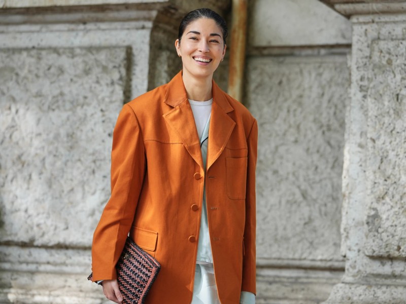 Model trägt einen orangefarbenen Blazer und hat ihre Haare zu einem Dutt gestylt.