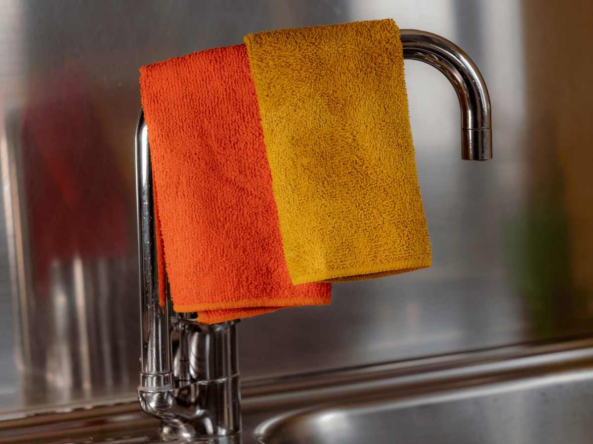 Gelber und Orangener Lappen trocknen auf dem Wasserhahn der K&uuml;chensp&uuml;le.
