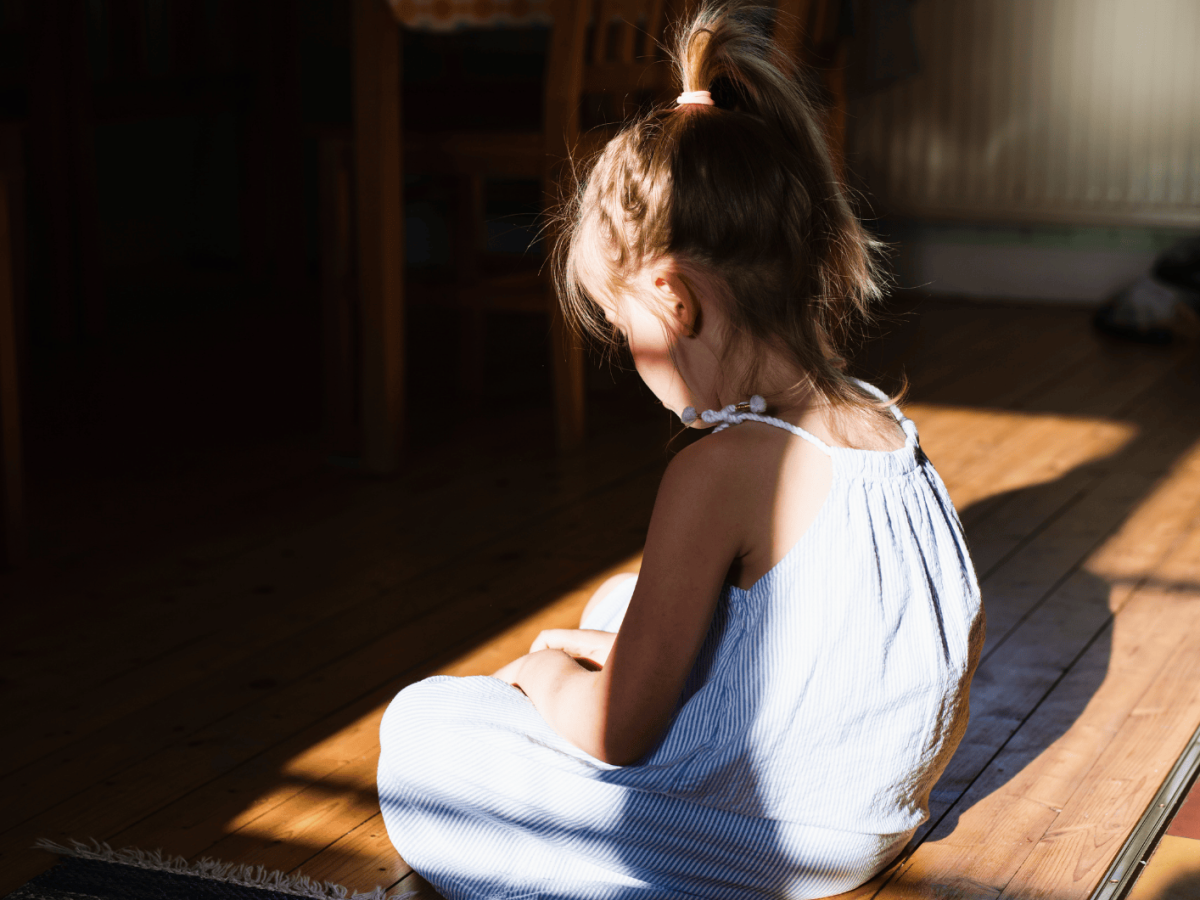 Kleines Mädchen sitzt alleine auf dem Küchenboden und schaut traurig nach unten.