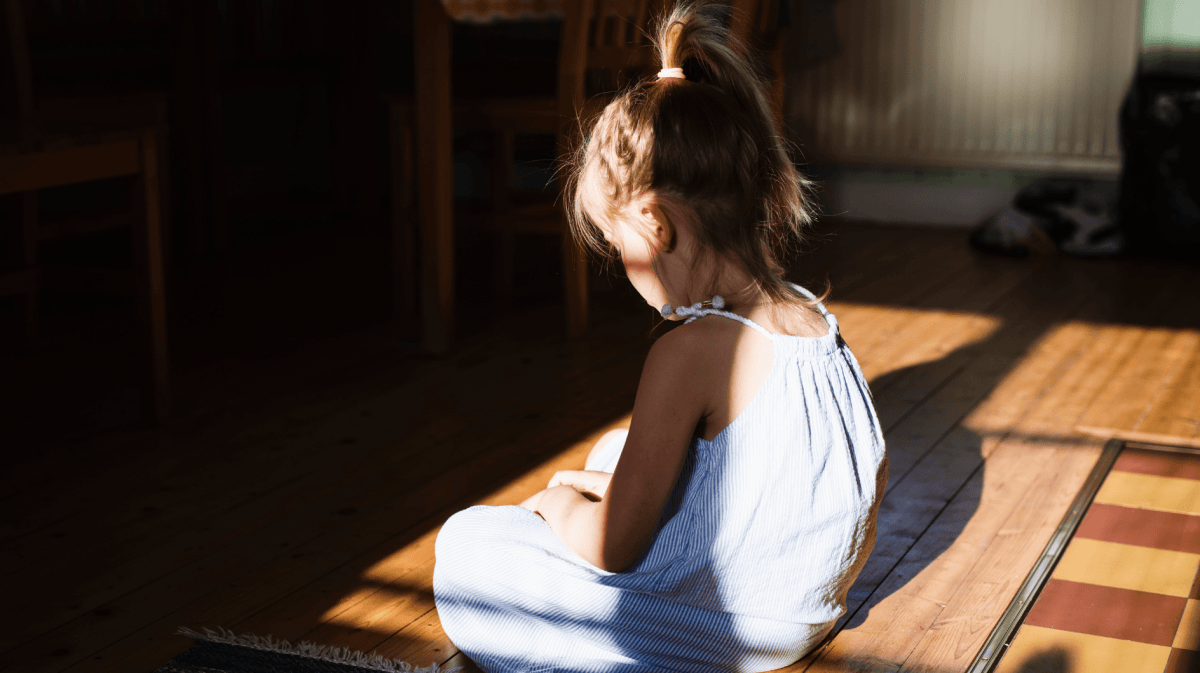 Kleines Mädchen sitzt alleine auf dem Küchenboden und schaut traurig nach unten.