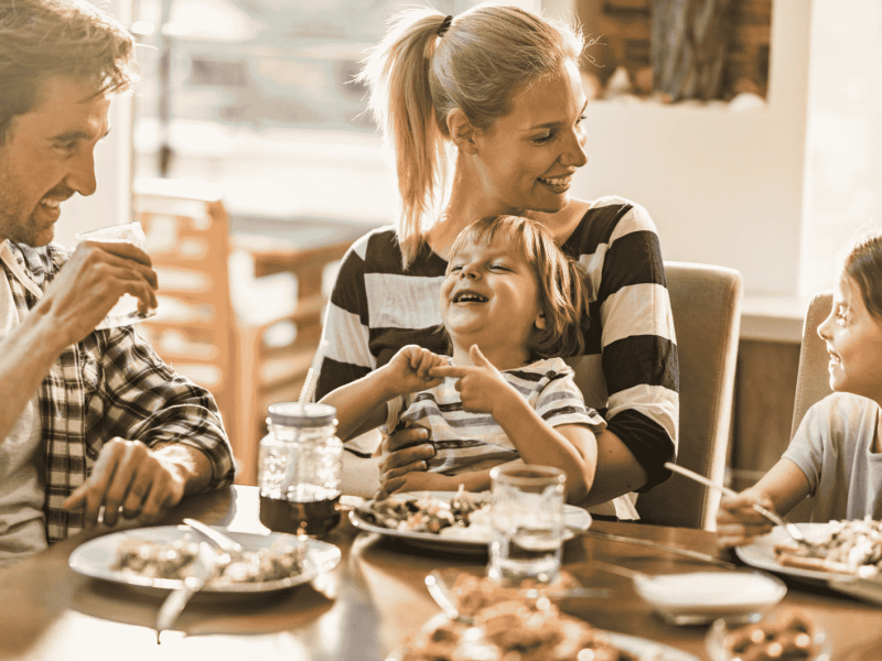 Familie mit zwei Kindern sitzt am Esstisch und lacht.