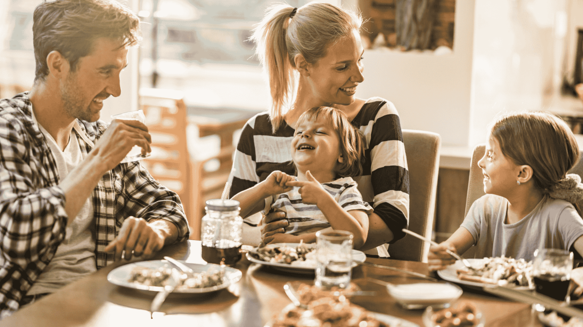 Familie mit zwei Kindern sitzt am Esstisch und lacht.