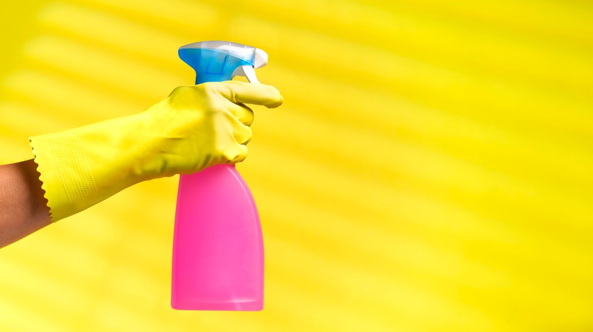 Hand in gelbem Gummihandschuh hält Reiniger