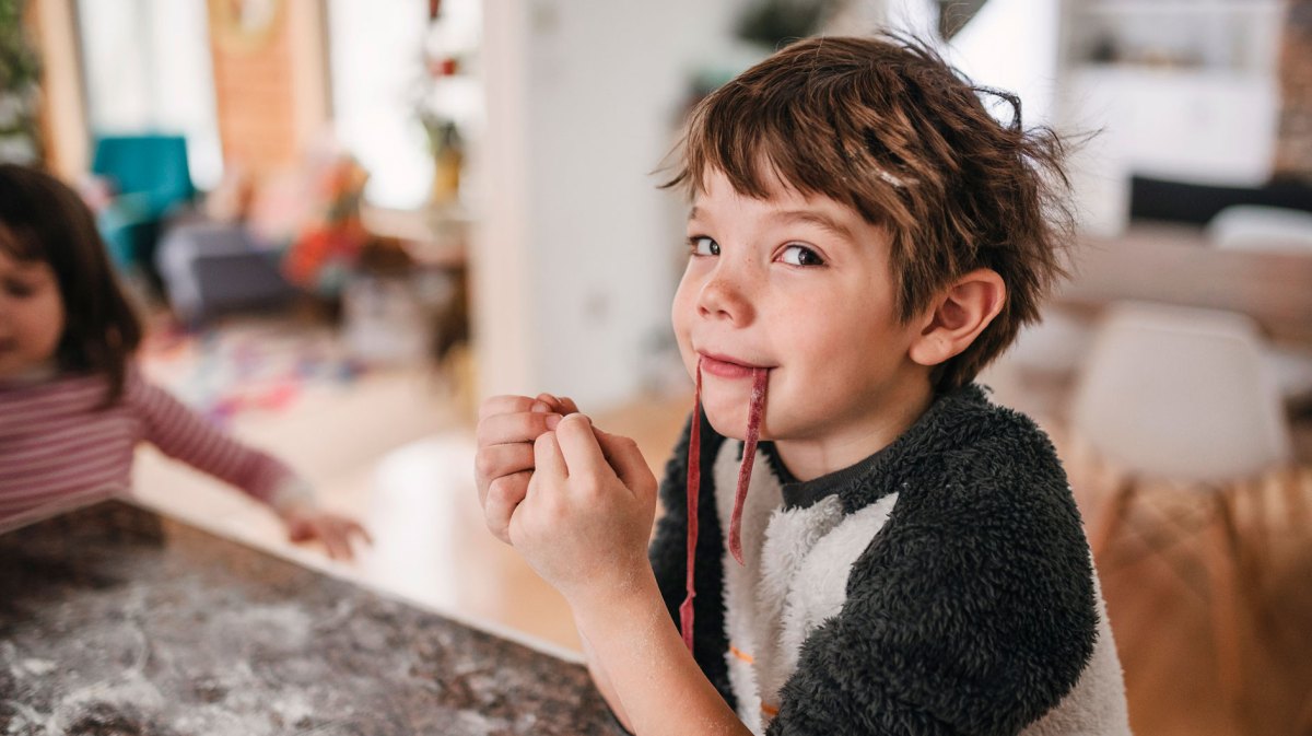 Porträt eines Jungen, der in der Küche sitzt und frische Pasta isst.