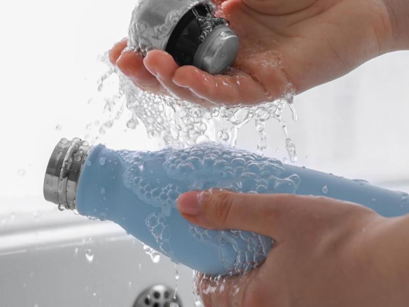 Frau spült eine Thermoskanne mit Wasser aus.