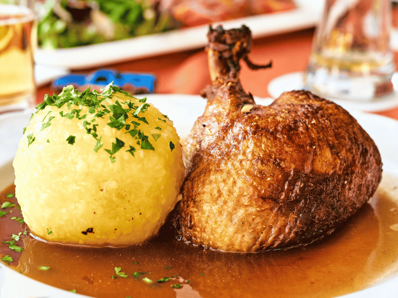 Großer Kartoffelkloß neben gebratener Entenkeule auf weißem Teller.