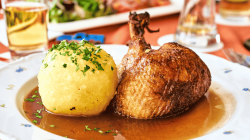 Gro&szlig;er Kartoffelklo&szlig; neben gebratener Entenkeule auf wei&szlig;em Teller.