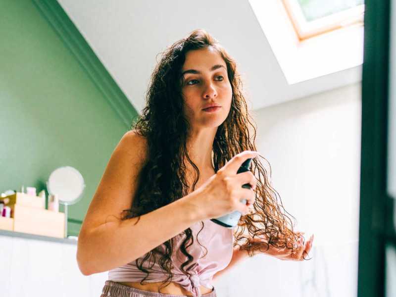Frau sprüht sich etwas in ihre frisch gewaschenen Haare.