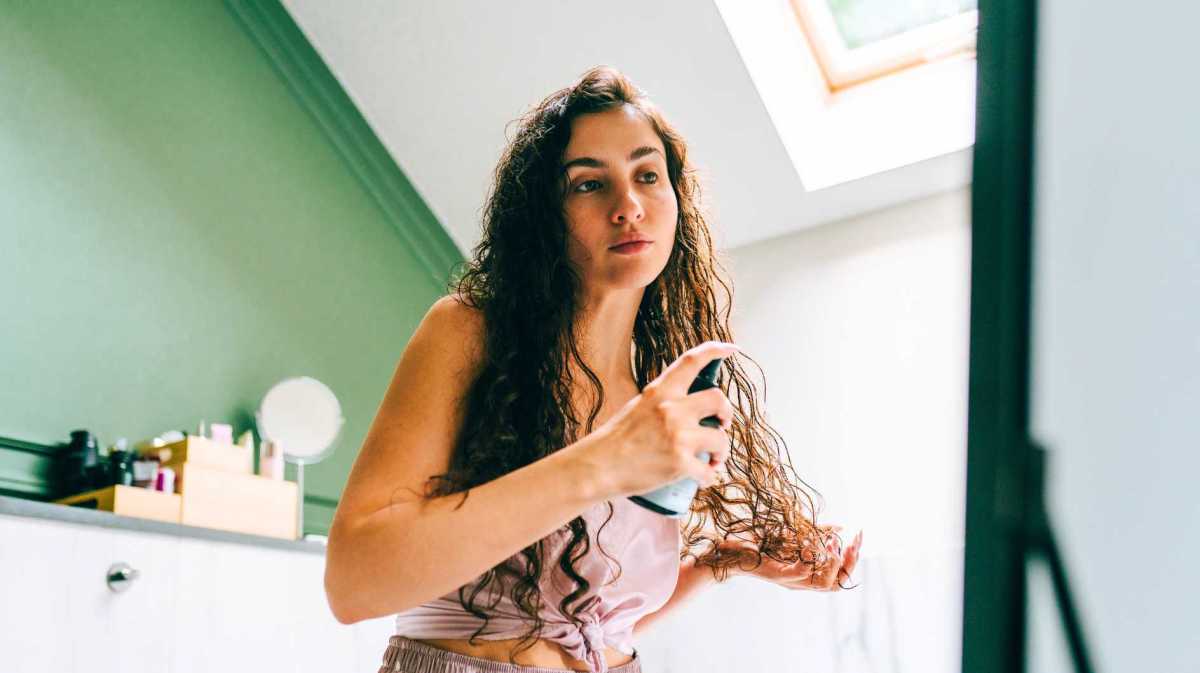 Frau sprüht sich etwas in ihre frisch gewaschenen Haare.