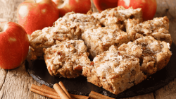 Apfel-Zimt-Kuchen auf einem Holztisch neben Äpfeln und Zimtstangen.