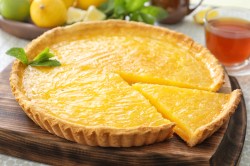 Eine Zitronentarte auf einem Holzbrett angerichtet.