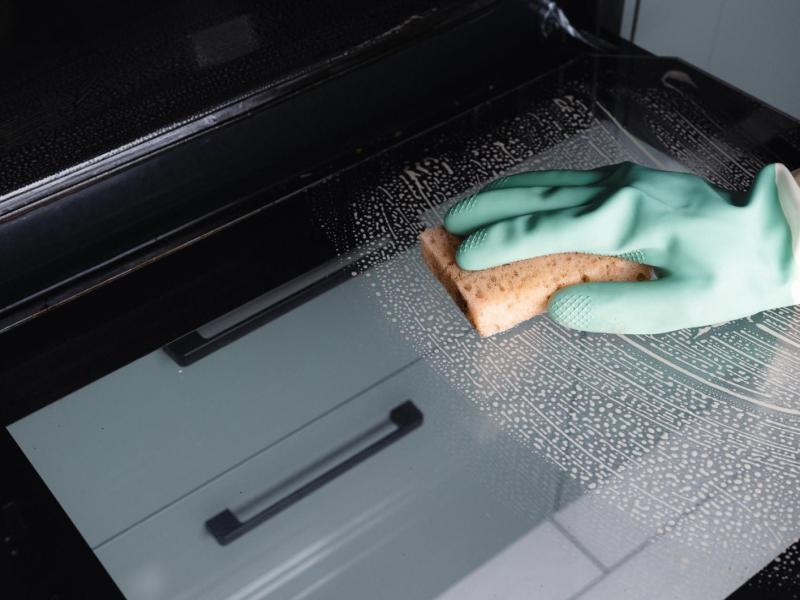 Person reinigt mit einem Handschuh und einem Schwamm den Backofen.