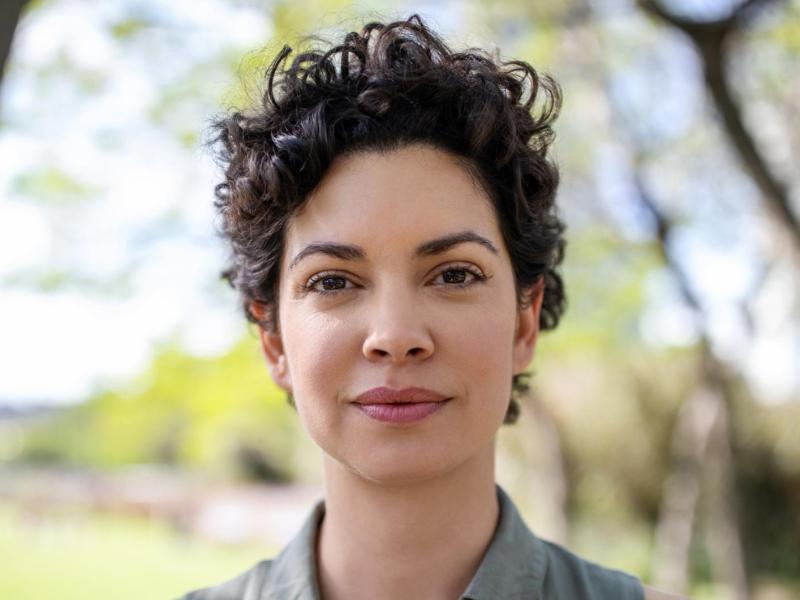 Junge Frau mit dunklen kurzer trendiger Locken-Frisur blickt selbstbewusst in die Kamera.