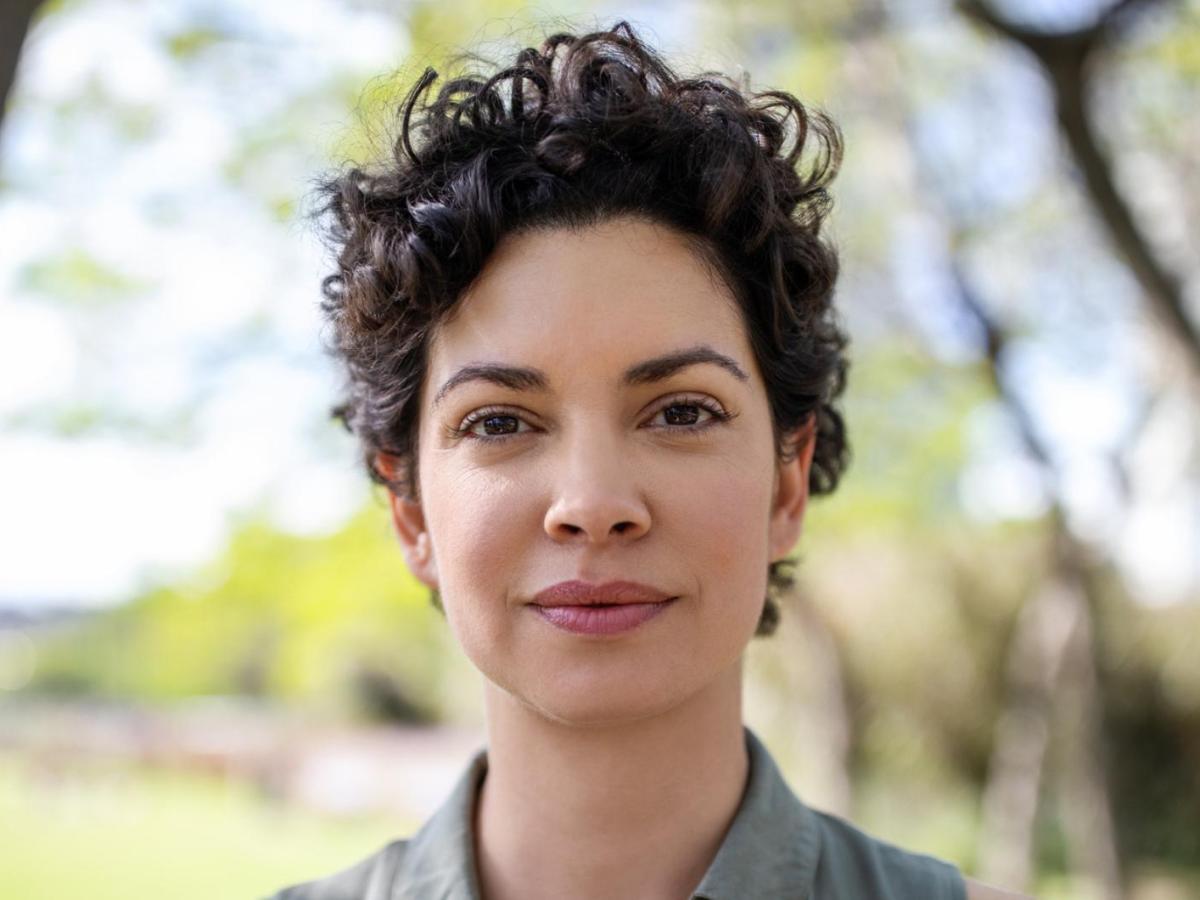 Junge Frau mit dunklen kurzer trendiger Locken-Frisur blickt selbstbewusst in die Kamera.