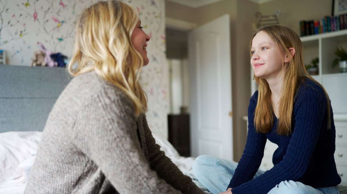 Mutter und Tochter sitzen im Zimmer des Teens auf dem Bett und unterhalten sich entspannt.