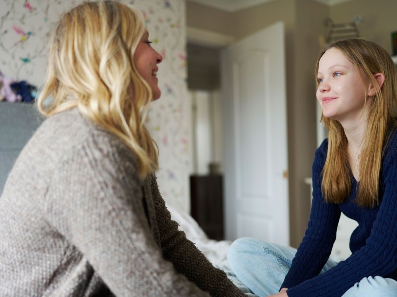 Mutter und Tochter sitzen im Zimmer des Teens auf dem Bett und unterhalten sich entspannt.