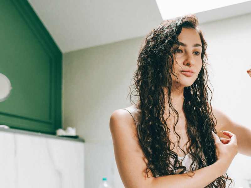 Frau, die ihre lockigen Haare nach dem Waschen stylt.
