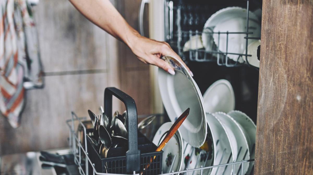 Person räumt Geschirr in die Spülmaschine ein.