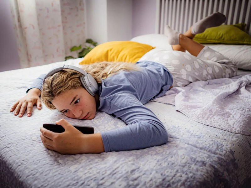 Teenagermädchen liegt faul auf ihrem Bett und schaut etwas auf seinem Handy.