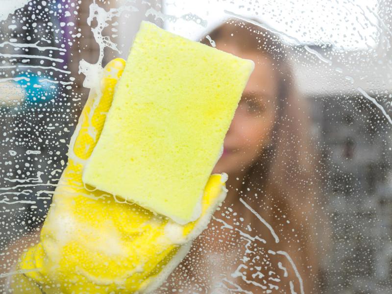 Frau putzt Duschwände mit einem Schwamm