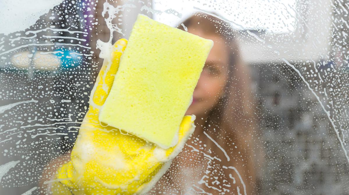 Frau putzt Duschwände mit einem Schwamm