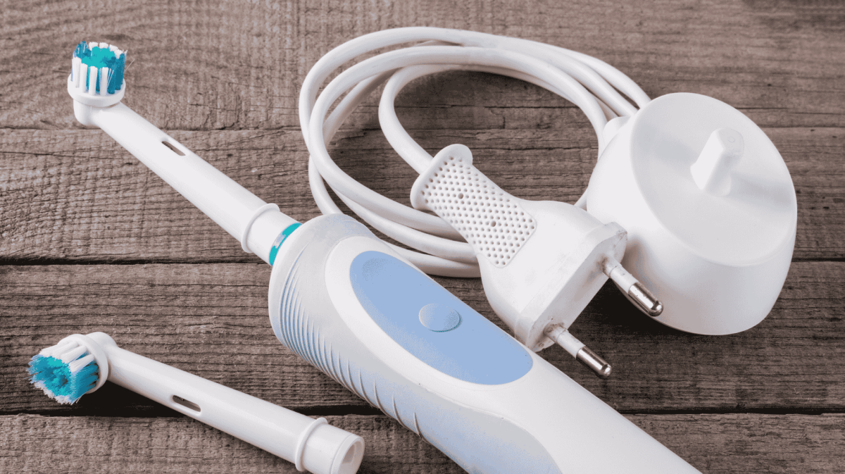 Elektrische Zahnbürste und Ladestation liegen auf Holztisch.