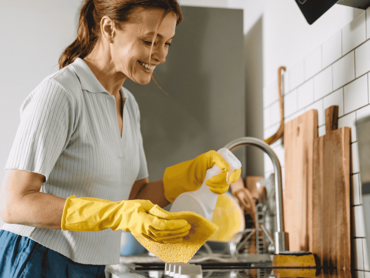 &Auml;ltere Frau putzt K&uuml;che, tr&auml;gt dabei gelbe Putzhandschuhe.