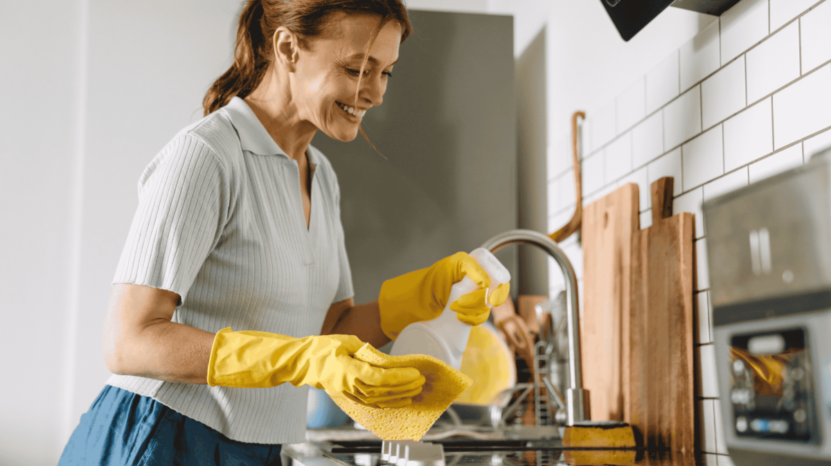 Ältere Frau putzt Küche, trägt dabei gelbe Putzhandschuhe.
