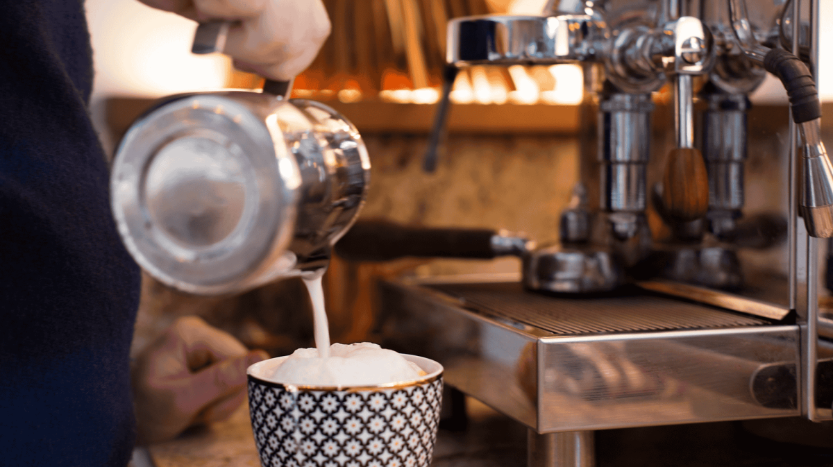 Milchschaum wird in eine bunte Tasse gegossen