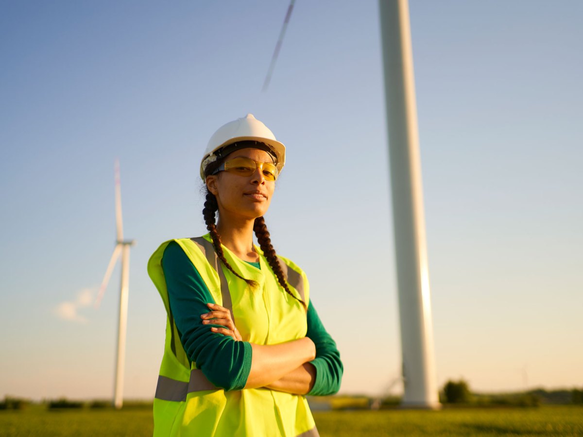 Frau in Arbeitskleidung vor zwei Windrädern.
