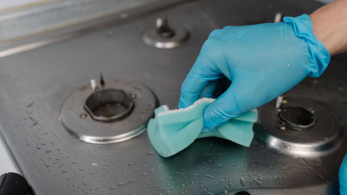 Person reinigt einen Herd mit einem Schwamm.