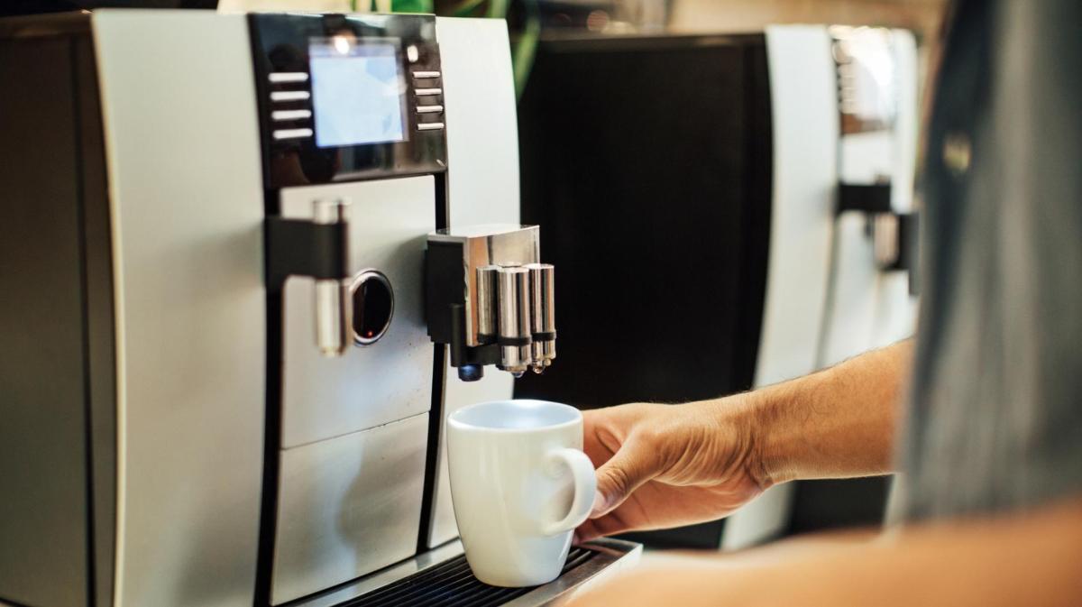 Mann stellt eine Tasse in einen Kaffeevollautomat .
