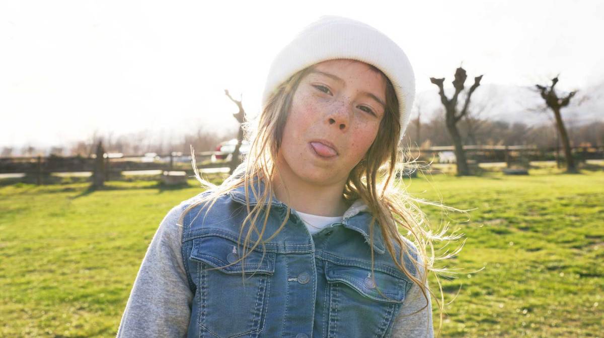 Mädchen an einem schönen Herbsttag draußen, streckt frech die Zunge raus.